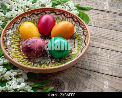 Eine Nahaufnahme mit Ostereiern in einer Schüssel auf einem Holztisch mit Blumen Stockfoto