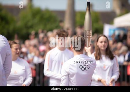 Ein Mann passiert die Olympische Flamme von Paris 2024 auf dem Stadtplatz in Sainte-Mère-Eglise, Normandie, als Teil des Relais de La Flamme vom 31. Mai 2024. Fackelträger marschierten durch das Dorf, als die Feierlichkeiten vor dem D-Day 80 stattfanden. Gedenkveranstaltungen wie diese dienen dazu, die Opfer zu ehren, die US-Mitglieder vor 80 Jahren zur Sicherung von Frieden und Sicherheit gebracht haben, und zukünftige Generationen dazu zu inspirieren, eine kollektive Vision des Weltfriedens zu schätzen. Stockfoto