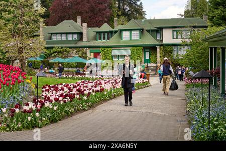 Menschen laufen auf dem Weg zwischen farbenfrohen Blumenbeeten zum Restaurant in Butchart Gardens, Victoria, BC. Stockfoto