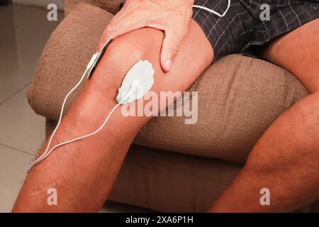 Ein Mann, der ein Elektrotherapie-Massagegerät oder eine TENS-Einheit am Knie zur Schmerzlinderung verwendet Stockfoto