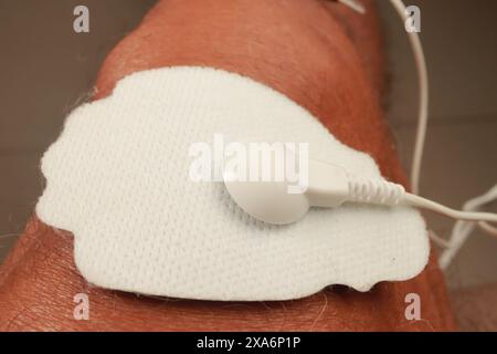 Ein Mann, der ein Elektrotherapie-Massagegerät oder eine TENS-Einheit am Knie zur Schmerzlinderung verwendet Stockfoto