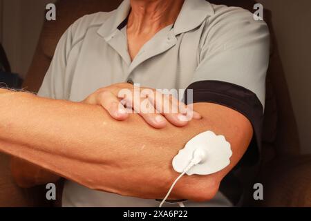 Ein Mann, der ein Elektrotherapie-Massagegerät oder TENS-Einheit am Ellenbogen benutzt Stockfoto