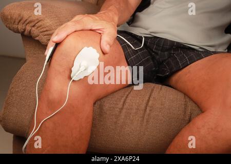 Ein Mann, der ein Elektrotherapie-Massagegerät oder eine TENS-Einheit am Knie zur Schmerzlinderung verwendet Stockfoto