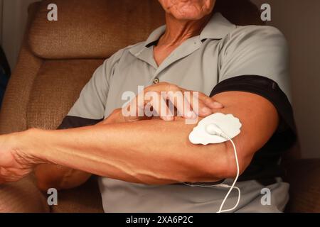 Ein Mann, der ein Elektrotherapie-Massagegerät oder TENS-Einheit am Ellenbogen benutzt Stockfoto