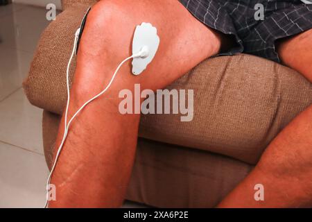 Ein Mann, der ein Elektrotherapie-Massagegerät oder eine TENS-Einheit am Knie zur Schmerzlinderung verwendet Stockfoto