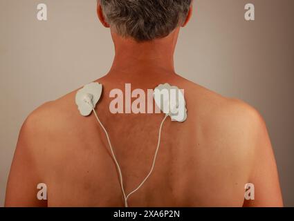 Ein Mann, der ein Elektrotherapie-Massagegerät oder eine TENS-Einheit auf dem Rücken zur Schmerzlinderung benutzt Stockfoto