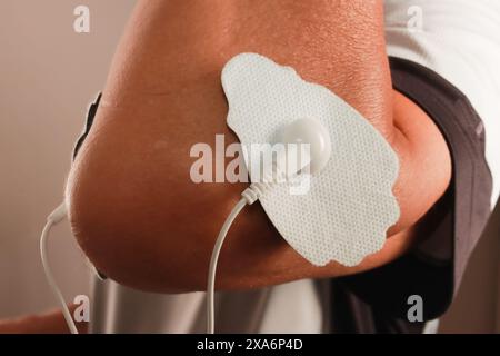 Ein Mann, der ein Elektrotherapie-Massagegerät oder TENS-Einheit am Ellenbogen benutzt Stockfoto