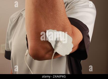 Ein Mann, der ein Elektrotherapie-Massagegerät oder TENS-Einheit am Ellenbogen benutzt Stockfoto