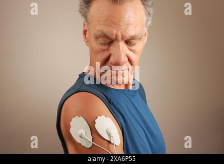 Ein Mann, der ein Elektrotherapie-Massagegerät oder TENS-Einheit auf seinem Deltamuskel verwendet, um Schmerzen für Muskeln und Gelenke zu lindern Stockfoto