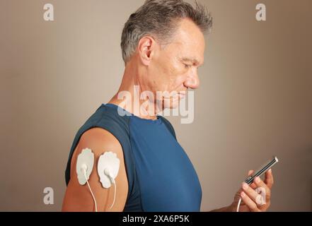 Ein Mann, der ein Elektrotherapie-Massagegerät oder TENS-Einheit auf seinem Deltamuskel verwendet, um Schmerzen für Muskeln und Gelenke zu lindern Stockfoto