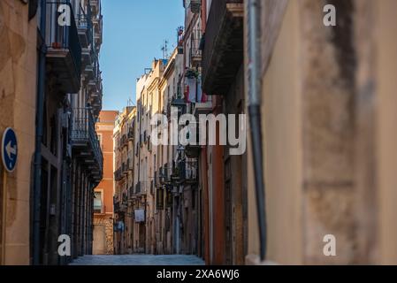 Spaziergang durch eine enge Straße mit bezaubernden historischen Gebäuden und Balkonen unter einem klaren Himmel, Tarragona Spanien Stockfoto