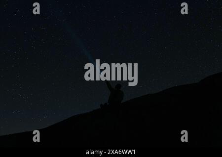 Helle Sterne und Sternbilder am Nachthimmel die Silhouette eines Mannes vor dem Hintergrund des Sternenhimmels Ein Mann strahlt eine Laterne in den Himmel Stockfoto