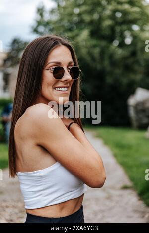 Ein Porträt einer fröhlichen jungen Frau in weißem Crop Top und Sonnenbrille. Stockfoto