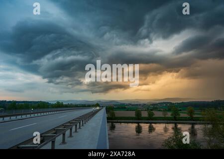 Über einer Brücke über einem Fluss, umgeben von Bäumen, erhebt sich ein malerischer Blick auf dunkle Wolken Stockfoto