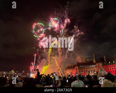 Eine große Gruppe von Zuschauern, die ein Feuerwerk in der Nähe eines Riesenrades beobachten Stockfoto