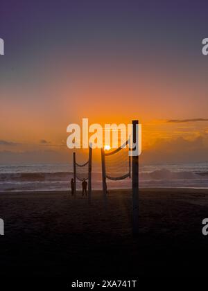 Sonnenuntergang hinter einem Beachvolleyballnetz mit Leuten im Hintergrund Stockfoto