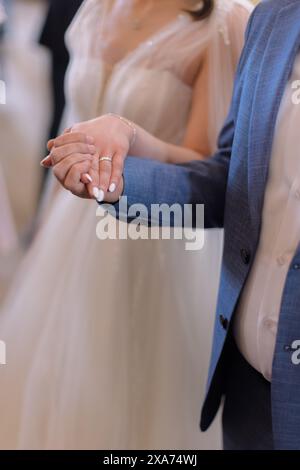 Ein Mann in blauem Anzug, der die Hand einer Frau hält, mit einem Ring in weißem Kleid und einem Ring Stockfoto