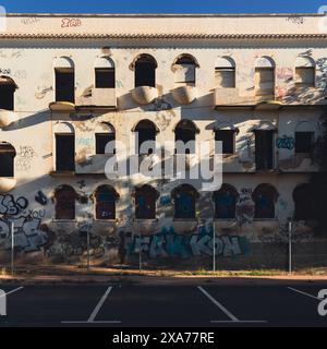 Graffiti-bedeckte Wand eines wunderschönen alten Gebäudes in der Nähe von Zaun und Parkplatz Stockfoto