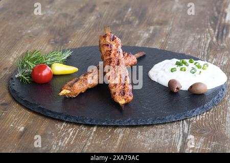 Ein Nahaufnahme eines Hackfleischspießes mit weißer Sauce und Beilagen auf einem rustikalen Tisch Stockfoto