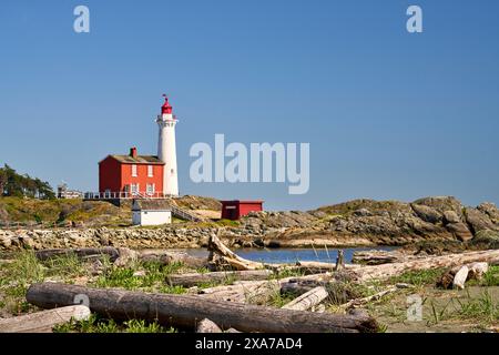 Blick auf den historischen, restaurierten Fisgard Lighthouse von einem mit Holzbäumen überdachten Strand. Stockfoto