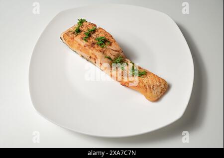 Ein gegrilltes Lachsfilet garniert mit frischem Dill, serviert auf einem makellos weißen Teller. Stockfoto