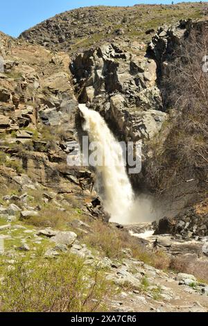 An einem sonnigen Frühlingstag fließt ein stürmischer Fluss eines Wasserfalls in einem schnellen Bach aus einer Spalte in den Bergen. Wasserfall Kurkure, Altai, Sibirien, Russi Stockfoto