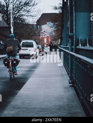 Ein stimmungsvolles Bild eines Radfahrers, der an einem regnerischen Tag auf einer Brücke in Deutschland fährt Stockfoto