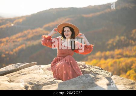Eine Frau in einem rosa Kleid, die auf einem großen Felsen steht, mit Bergen im Hintergrund Stockfoto