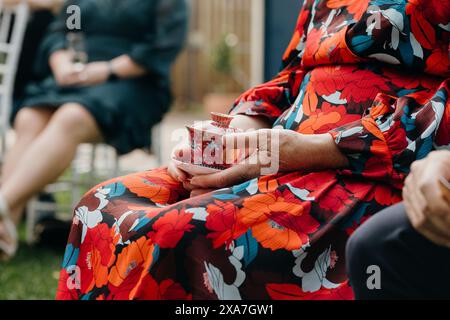 Eine Frau in einem Blumenkleid am Hochzeitstag, die eine Tasse hält Stockfoto