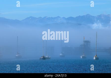 Mehrere Boote segeln auf nebelhaltigen Gewässern vor einem Hintergrund von Bergen Stockfoto