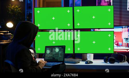 Mann, der Code auf Laptop vor isolierten Bildschirm-PC-Monitoren schreibt und versucht, an Sicherheitssystemen vorbei zu kommen. Hacker verwenden Chroma Key Computer und Notebook, um Skripte zu erstellen, die Geräte, Kamera A, hacken können Stockfoto