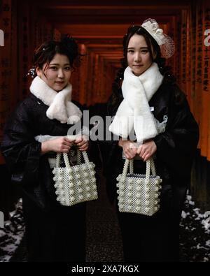 Zwei junge japanische Frauen in formeller Winterkleidung posieren vor dem Torii Gate Tunnel am Fushimi Inari Schrein in Kyoto Japan. Stockfoto