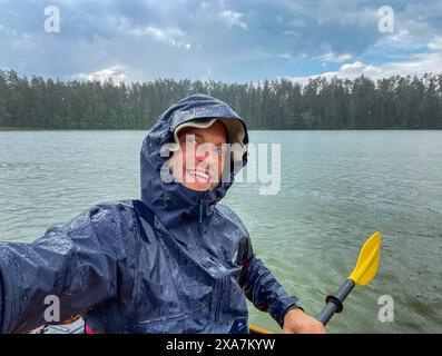 Eine Person im Regenmantel, die Kanu auf dem Wasser im Fluss Czarna Hancza in Polen paddelt Stockfoto