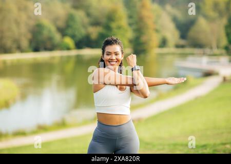 Junge Frau streckt Arm in Park nahe Scenic Lake Stockfoto