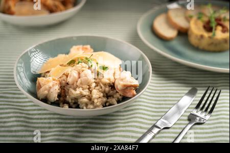 spanisches Paella-Gericht. Fisch- und Hühnerrisotto auf blauem Teller. Reis, Garnelen und Huhn. Serviert auf dem Tisch mit Gabel und Messer Stockfoto