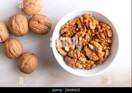 Walnüsse in einer weißen Schüssel auf einem Marmorteller. Geschälte und getrocknete Hälften von Walnusskernen, reife Samen des gewöhnlichen Walnussbaums Juglans regia. Stockfoto