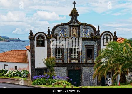 Historische Kirche Kloster von Caloura an der Küste mit blauen und weißen Fliesen und Meerblick, umgeben von Blumen und einer Palme, Fischerdorf Stockfoto