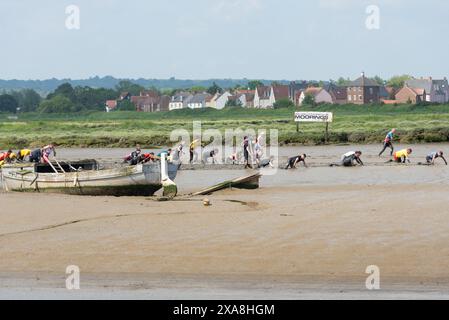 Teilnehmer am Maldon Mud Race in Maldon, Essex, Großbritannien, im Schlamm des Flusses Chelmer. Die Teilnehmer krabbeln im Schlamm auf der Ferne von alten Booten Stockfoto