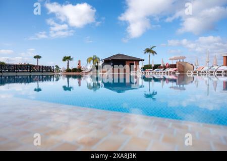 Ein Pool mit einem kleinen Gebäude im Hintergrund. Der Pool ist von Liegestühlen und Sonnenschirmen umgeben Stockfoto