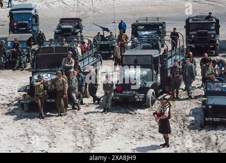 D Day Re-enactment an den Stränden der Normandie in Nordfrankreich, Juni 1979. Bilder gescannt 2019 Piper Bill Millin am Omaha Beach mit Oldtimer-Militärfahrzeugen. Piper Millen – William 'Bill' Millin (* 14. Juli 1922 bis 17. August 2010) war persönlicher Piper von Simon Fraser, 15. Lord Lovat, Kommandeur der 1 Special Service Brigade am D-Day. Millin ist am besten bekannt dafür, dass er während der D-Day Landung in der Normandie Pfeifen spielte, während er unter Feuer stand. Pipers wurden traditionell in der Schlacht von schottischen und irischen Soldaten eingesetzt, jedoch beschränkte sich der Einsatz von Dudelsacksäcken auf den hinteren Bereich Stockfoto