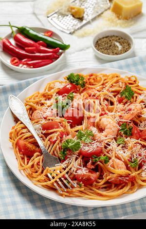 Garnelen fra diavolo mit Spaghetti, Tomatensoße, bestreut mit geriebenem Parmesankäse auf weißer Platte auf weißem Holztisch mit Gabel, vertikal Stockfoto