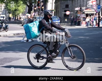 Deliveroo-Fahrer auf dem E-Bike über die Straße im Zentrum Londons Stockfoto