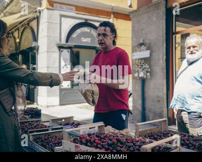 Cremona, Italien - 27. Mai 2024 Frau kauft frische Kirschen auf dem Markt. Sie übergibt Geld an den Verkäufer, der die Früchte in ein Braun bringt Stockfoto