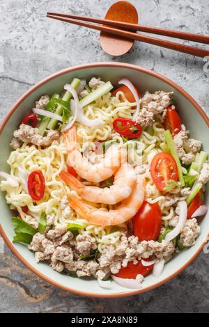 Scharfer Salat aus Instant-Nudeln, Garnelen, Schweinefleisch, Gemüse und heißer Soße Dressing typisch thailändische Gerichte aus der Nähe auf dem Teller auf dem Marmortisch. Vertic Stockfoto