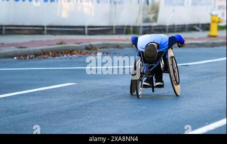 Ein junger Mann im Rollstuhl, der die Straße entlang fährt, während er an einem Marathon auf Long Island in New York teilnimmt. Stockfoto