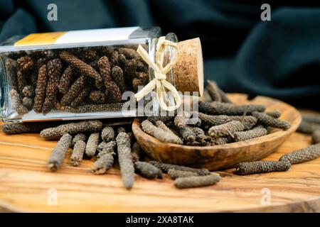 Langer Pfeffer (Piper longum), auf Holzplatte mit Glas Stockfoto