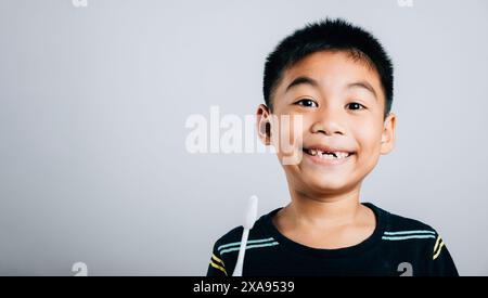 Isoliert auf weißem Hintergrund hält ein asiatischer Junge ohne oberen Milchzahn eine Zahnbürste Stockfoto