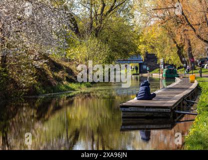 Edinburgh, Schottland; 23. April 2021: Union Canal im Frühjahr, am Harrison Park, mit bunten Bäumen, Menschen entlang des Weges und einem Mann, der auf dem Pier sitzt Stockfoto