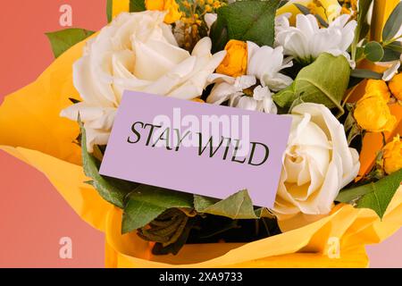 Finanzkonzept bedeutet „Stay Wild“ mit Inschrift auf einer lila Visitenkarte in einem Blumenstrauß aus zarten Rosen Stockfoto