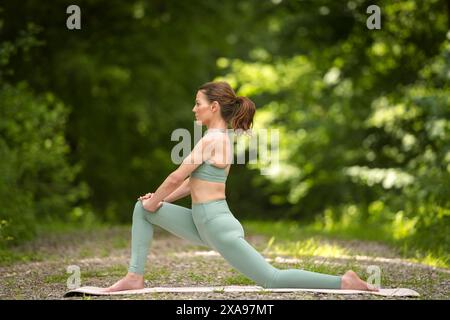 Sportliche Frau, die Yoga im Park macht, Dehnübungen, niedriger Ausfallschritt. Stockfoto